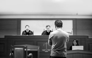 Black and white photo of a man standing in front of judges. His back is to the camera.